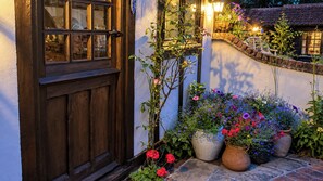 Une porte en bois avec une fenêtre, des plantes en pot fleuries et un mur de pierre.