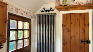 Une pièce dotée d’une porte en bois, d’un radiateur et d’une fenêtre donnant sur un espace verdoyant.