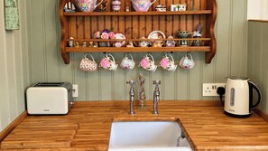 Une cuisine avec un plan de travail en bois, un évier, un grille-pain, une bouilloire et une étagère ornée d’objets décoratifs.
