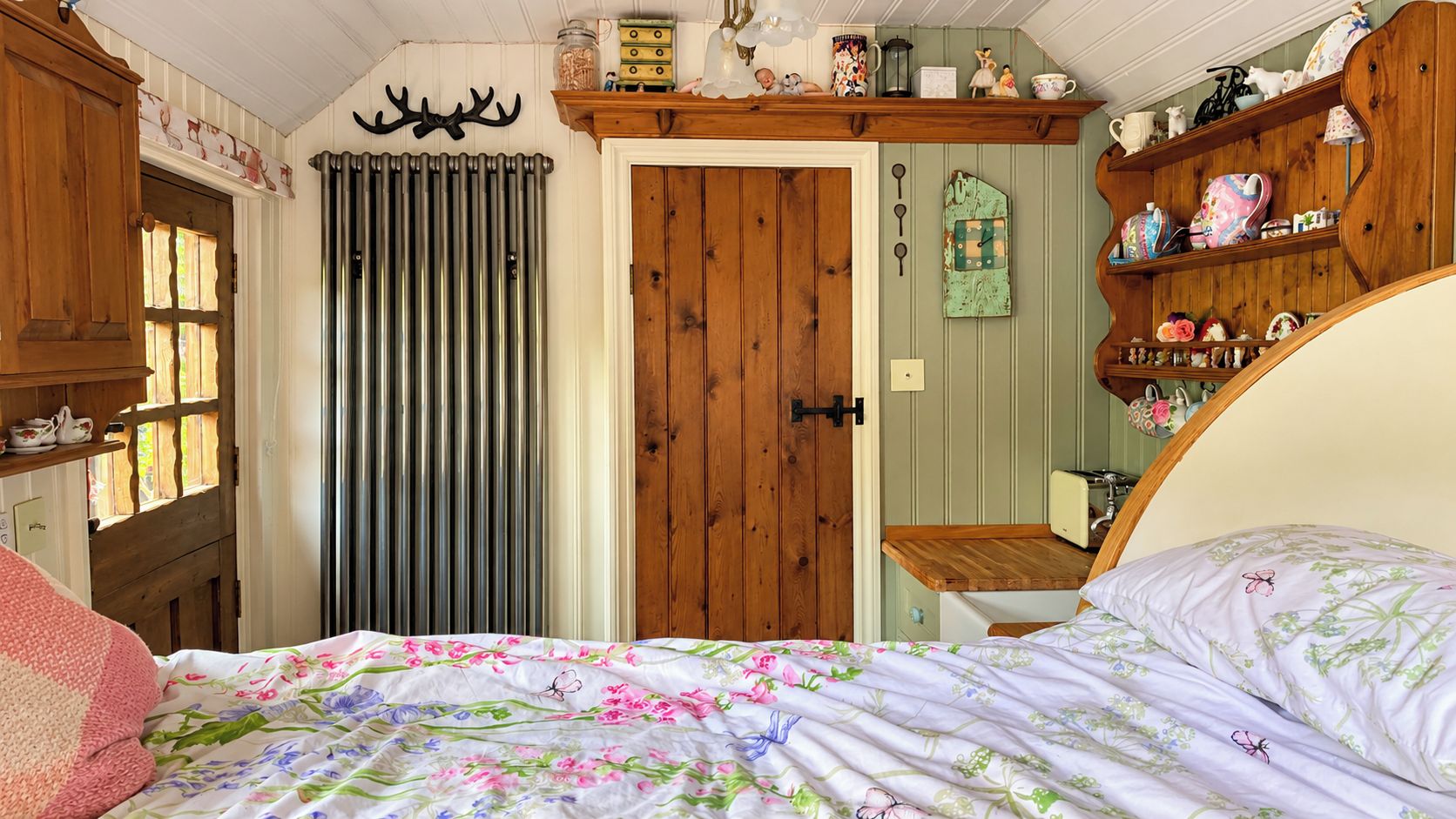 A bedroom with a bed, wooden door, radiator, and shelves with various items.