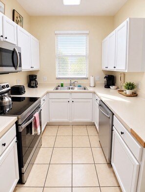 A compact kitchen with white cabinets, a microwave, a stove, a dishwasher, and a window with blinds. - 4BR/3BA Disney Retreat Pool & Lazy River/Patio/ lFitness rm Near all attractions (Davenport)