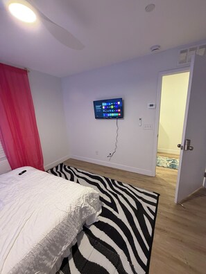 Une chambre à coucher avec un lit, un tapis à motifs zébrés, un téléviseur fixé au mur et une porte donnant sur une autre pièce.