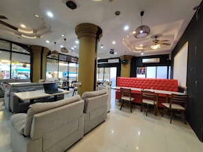 L’intérieur d’un restaurant, avec différents types de sièges, notamment un coin salon rouge et des canapés gris.