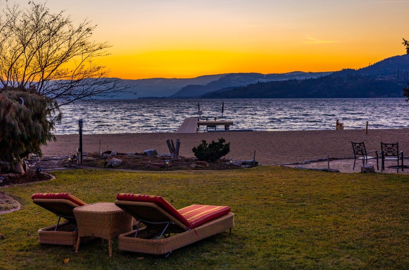 A beachside setting with lounge chairs, a wooden deck, and a view of the water and hills.