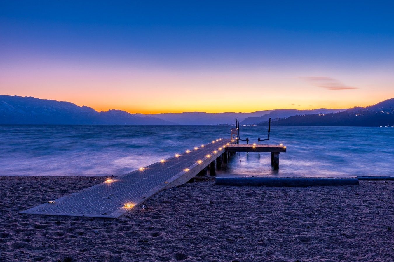 A wooden pier extending into calm waters with a sunset in the background.