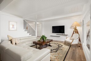 Uma sala de estar com sofá, mesa de centro, televisão e abajur.