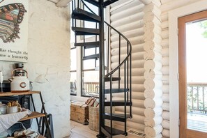 Un escalier en colimaçon à l’intérieur d’un chalet en bois, dans un style rustique, avec une cheminée et une vue sur l’extérieur.