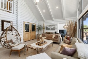 L’intérieur d’une cabane en rondins comprend un espace nuit en mezzanine, un coin repas et un salon aménagé avec un fauteuil suspendu, un canapé et une table basse.