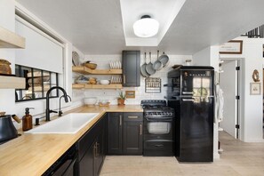 A modern kitchen with a black refrigerator, a stove, and a sink. There are wooden shelves above the sink and a window on the left. - Sedona Desert Sactuary: Boho-Chic Cabin for 16 on one acre with Red Rock Views (Sedona)