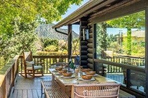 A wooden deck with a dining table set for six, surrounded by wicker chairs. - Sedona Desert Sactuary: Boho-Chic Cabin for 16 on one acre with Red Rock Views (Sedona)