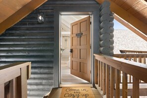 Un escalier en bois mène à une porte sur laquelle est posé un paillasson avec l’inscription : « Entrez, installez-vous confortablement ».