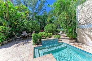 Ein Schwimmbecken, umgeben von üppiger Vegetation, mit einer Terrassenfläche und Gartenmöbeln.