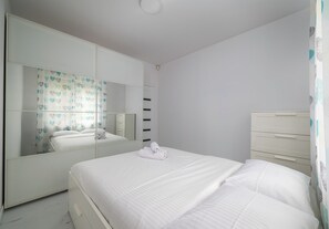 Un dormitorio con un espejo grande, una cama con ropa de cama blanca y un armario blanco.