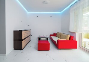 Una sala de estar moderna con un sofá rojo, un aparador de madera y una mesa de centro de vidrio.