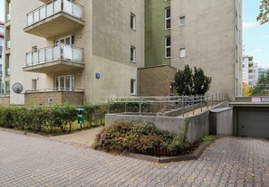 Un edificio residencial de varios pisos con balcones, un pequeño jardín y un sendero pavimentado.