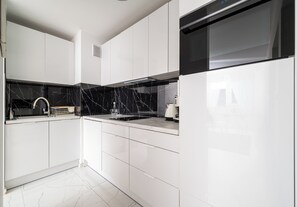 Une cuisine moderne avec des meubles blancs, un dosseret noir et une hotte de cuisinière en acier inoxydable.