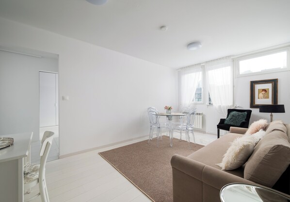 Un salon moderne avec un canapé beige, une table basse en verre et un coin repas doté de chaises transparentes.