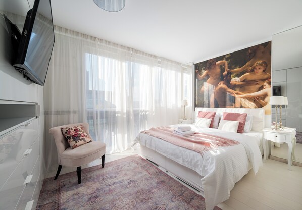 Habitación de hotel con una cama, una silla, un televisor y un cuadro grande en la pared.
