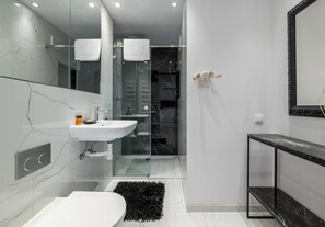 Un baño moderno con un lavamanos blanco, una cabina de ducha con mampara de vidrio y una encimera de mármol negro.