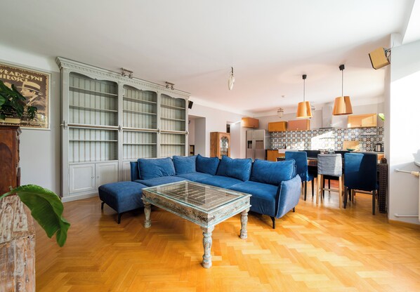 Una sala de estar con un sofá azul, una mesa de centro de vidrio y piso de madera.