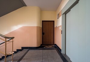 Un couloir avec une porte en bois, une main courante et un sol recouvert de moquette.