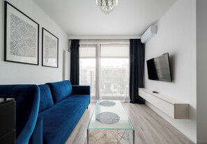 Un salon moderne avec un canapé bleu, une table basse en verre, un téléviseur à écran plat et deux tableaux encadrés accrochés au mur.