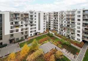 Un edificio residencial de gran altura con varios balcones, un patio central con árboles y un banco, y un área de estacionamiento.
