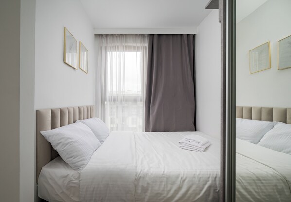 Une chambre d’hôtel avec un lit, une fenêtre avec des rideaux légers et des tableaux encadrés accrochés au mur.
