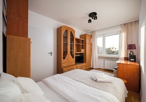 Une chambre à coucher avec un lit, une armoire en bois, une télévision et une fenêtre avec des rideaux.
