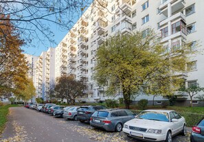 Fila de autos estacionados a lo largo de una calle arbolada junto a un edificio residencial de varios pisos.