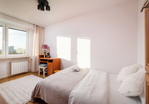 Un dormitorio con cama, escritorio, silla, radiador y ventana.