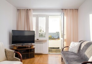 Una sala de estar con un televisor de pantalla plana sobre un soporte de madera, un sofá con un cojín mullido y una silla con un cojín estampado.