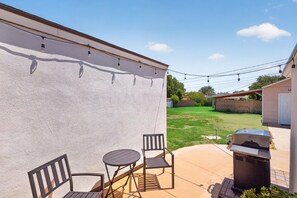 Eine Terrassenfläche mit Tisch, Stühlen, einem Grill und einer Lichterkette.
