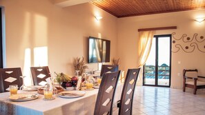 Un comedor con una mesa dispuesta para dos personas, un televisor montado en la pared y vistas al exterior a través de un ventanal.