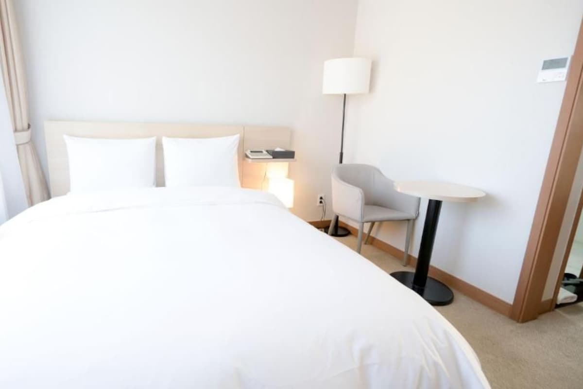 A hotel room with a large bed, a bedside table, a chair, and a lamp.