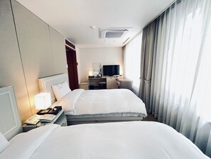 A hotel room with two beds, a desk with a television, a phone, and a window with curtains. - Hotel Yeongildae (Pohang)