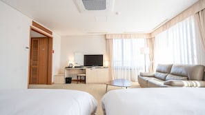 A hotel room with two beds, a desk with a TV, a sofa, and a window with curtains. - Hotel Yeongildae (Pohang)
