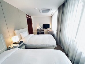 A hotel room with two beds, a desk, a chair, a television, and a window with curtains. - Hotel Yeongildae (Pohang)