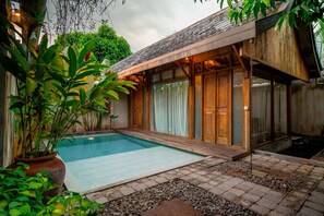A swimming pool with a wooden deck and a covered area with glass doors. - Ayom Java Village Solo (Karanganyar)