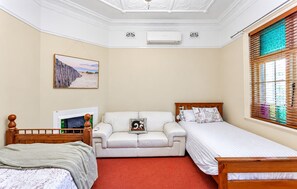 Een slaapkamer met een bed, een slaapbank, een televisie en een raam met zonwering.