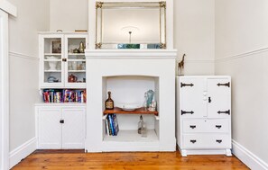 Een kamer met een open haard, boekenkasten, een kast en een decoratieve spiegel.
