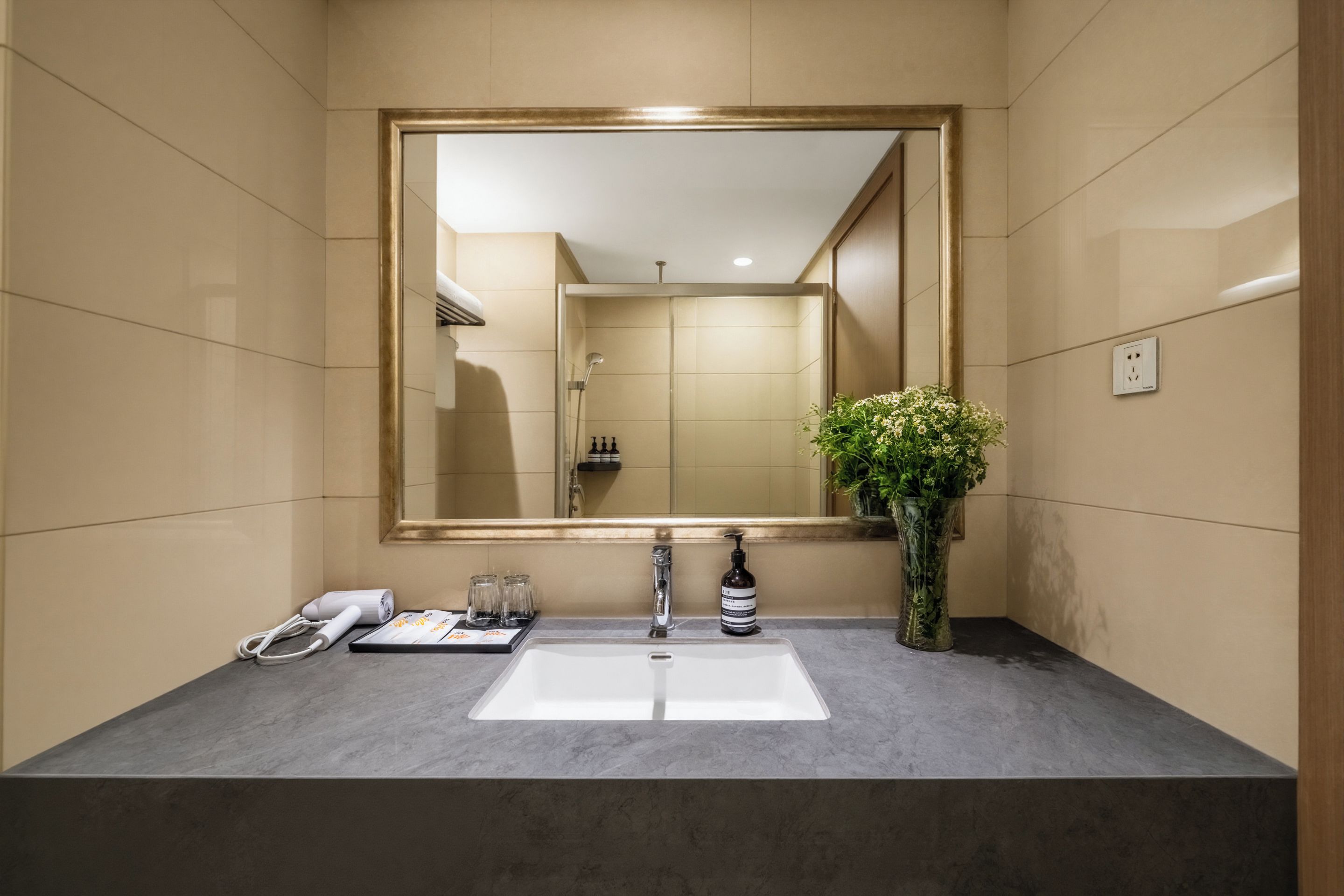 Un bany amb un mirall gran, un lavabo, una dutxa i un ram de flors.