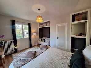 A bedroom with a bed, bedside tables, a radiator, a window with curtains, a hanging lamp, and built-in shelving. - New Listing (Jouy-le-Potier)