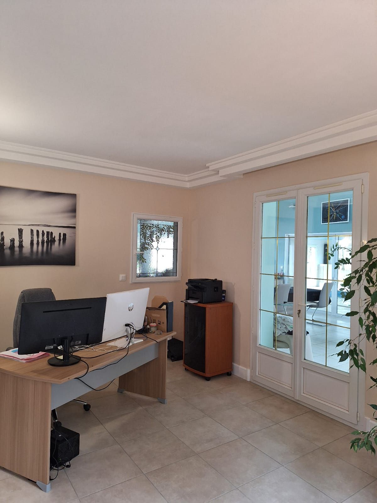 A room with a desk, computer, printer, and a window with a view of a building.
