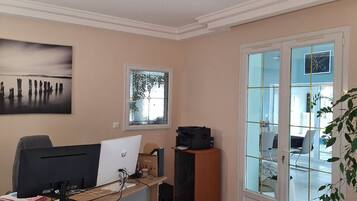 A room with a desk, computer, printer, and a window with a view of a building.