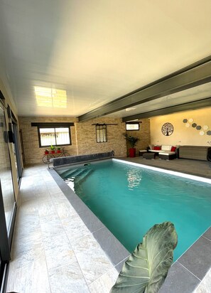 Una piscina interna con pavimento piastrellato, una panca e un muro decorato con un murale raffigurante un albero.