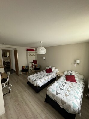 Habitació d'hotel amb dos llits, escriptori, cadira, armari i llum penjant.