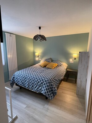 Una camera da letto con una coperta dal disegno vivace, due lampade sui comodini, una ventola a soffitto e un termosifone.