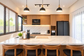 Eine moderne Küche mit Marmorarbeitsplatte, Holzschränken, einer eingebauten Mikrowelle, einem Kühlschrank und Pendelleuchten.