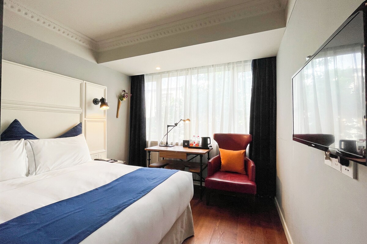 Quarto de hotel com cama, escrivaninha, cadeira e televisão.